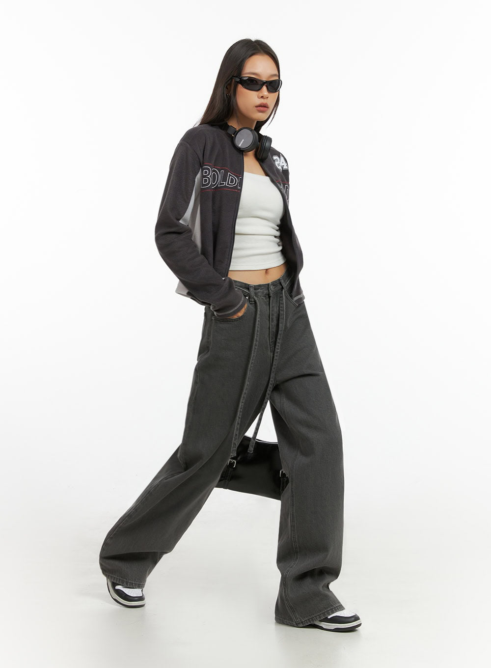 Emery Cotton Strap Baggy Jeans IO409 in dark gray, full-body walking shot on model, acubi street style paired with graphic varsity jacket, white tube top, and sneakers.