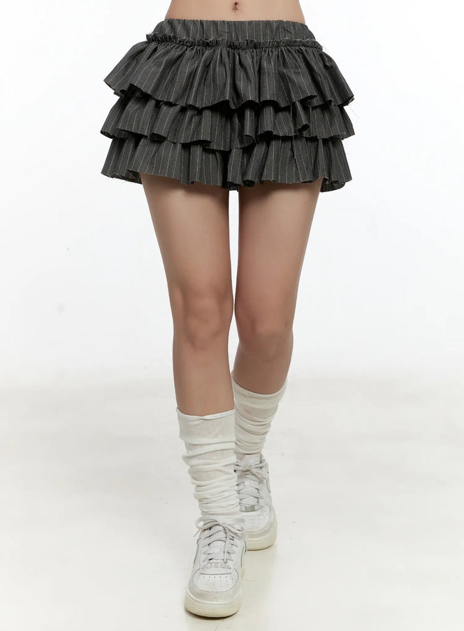 LEWKIN Striped Ruffle Mini Skirt CL531 in dark gray, front crop shot on model, three-tier pinstripe ruffles with elastic waistband, styled with white leg warmers and sneakers.