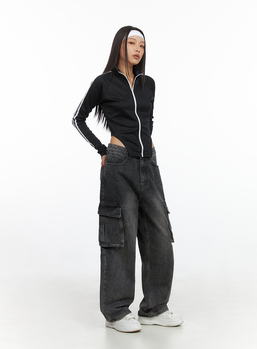 LEWKIN Neve Washed Cargo Denim Jeans IS427 in washed black, 3/4 front angle on model, wide-fit baggy cotton denim with cargo pockets, styled with black zip-up crop top and white sneakers.