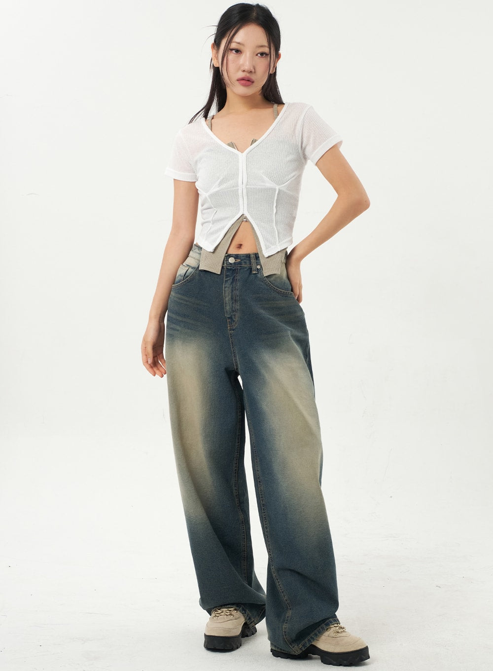 LEWKIN Mid-Rise Baggy Jeans CA325 in vintage blue denim, full-length front view on model, wide-leg silhouette with yellow-tinted fading, paired with white sheer crop top and chunky boots.