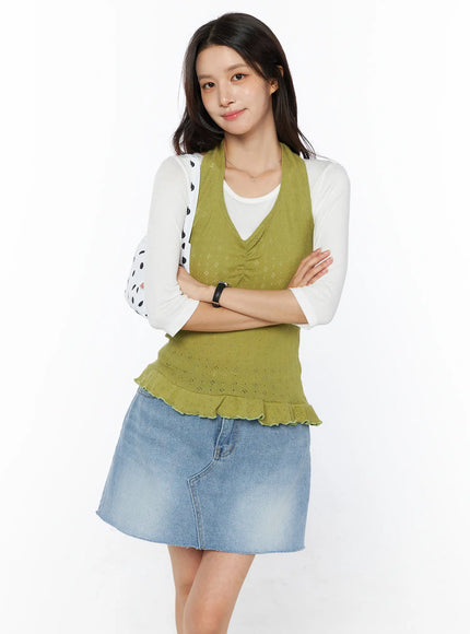 LEWKIN Frill Hem Halter Neck Top CU522 in green, front three-quarter view on model, arms crossed, pointelle knit with ruched V-neckline and frill hem, layered over white long-sleeve top with blue denim mini skirt.