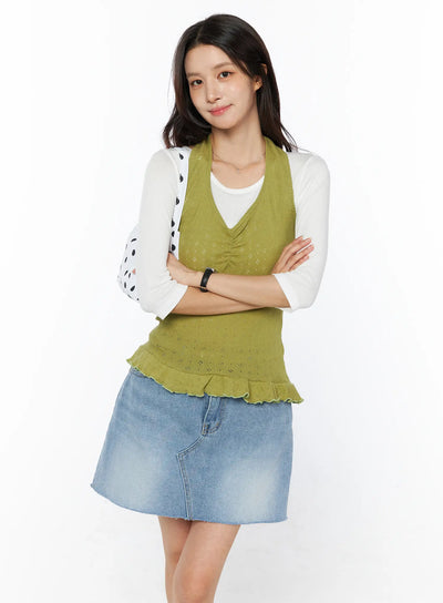 LEWKIN Frill Hem Halter Neck Top CU522 in green, front three-quarter view on model, arms crossed, pointelle knit with ruched V-neckline and frill hem, layered over white long-sleeve top with blue denim mini skirt.
