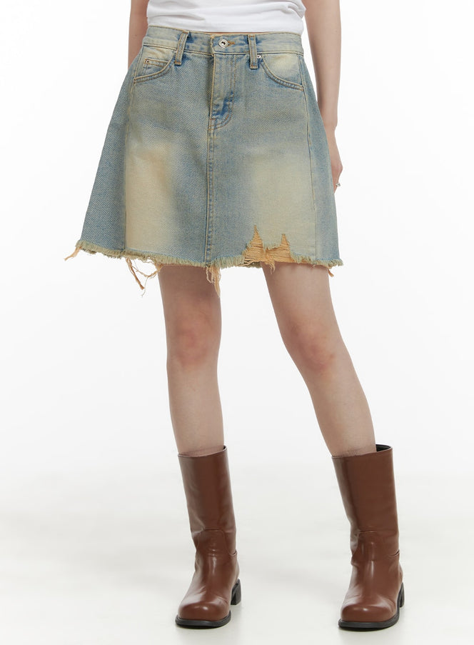 LEWKIN Vintage Destroyed Hem Mini Skirt CA418 in light blue, front view on model, washed cotton denim with destroyed frayed hem and yellow tint, paired with brown knee-high boots.