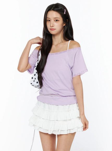 LEWKIN Lace Trim Off-Shoulder Tee CU522 in light purple, angled front view on model, off-shoulder lace neckline and lace cuff trim, styled with white ruffle mini skirt and polka-dot bag.
