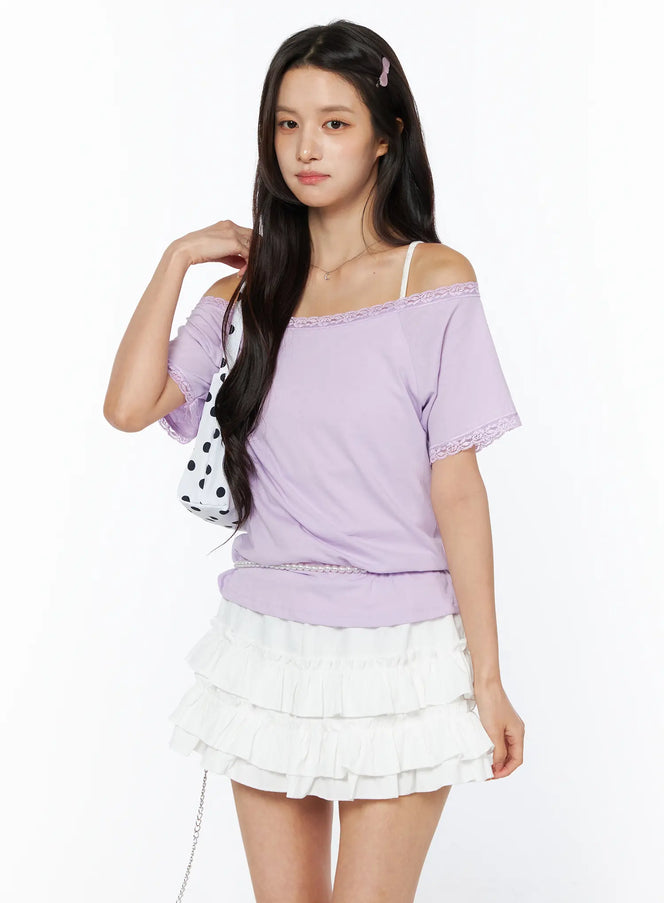 LEWKIN Lace Trim Off-Shoulder Tee CU522 in light purple, angled front view on model, off-shoulder lace neckline and lace cuff trim, styled with white ruffle mini skirt and polka-dot bag.