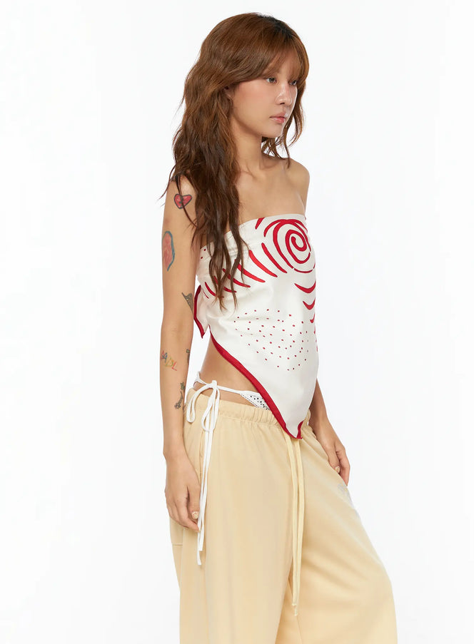 LEWKIN Red Swirl Print Scarf CU518 in red, side view on model styled as a bandeau tube top, cream polyester fabric with bold red swirl graphic and dot pattern, red border trim, paired with cream drawstring trousers.