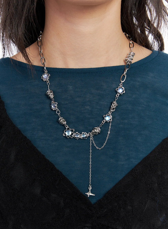 LEWKIN Blue Cubic Twist Necklace CC1809 in silver, close-up on model's neckline, blue cubic beads with twisted chain links and dangling star charm, styled over teal and black layered top.
