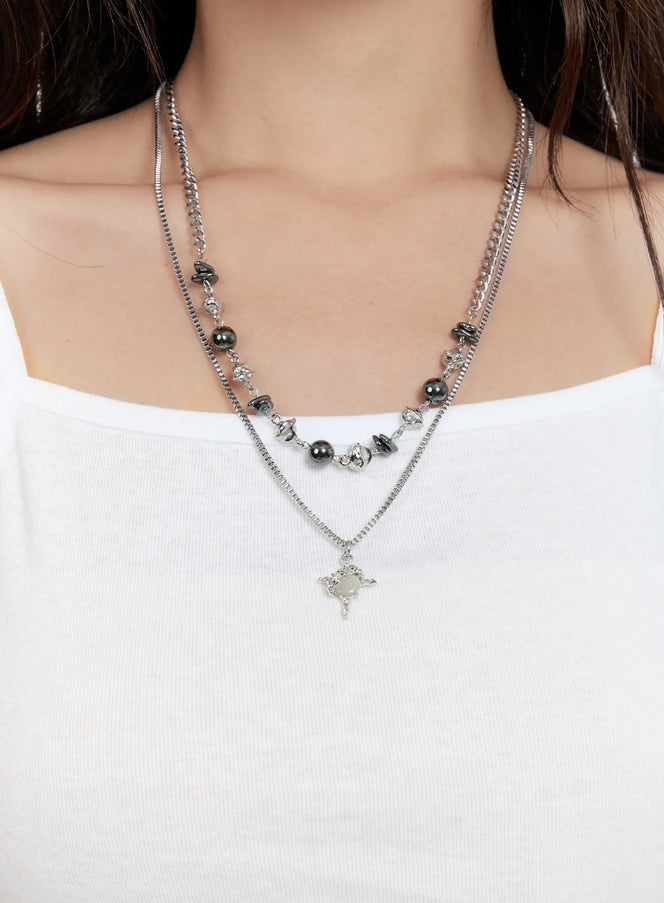 LEWKIN Layered Bead Necklace CG501 in silver, chest close-up on model, double-layer chain with dark hematite pearls and star cross pendant, worn over white ribbed cami.