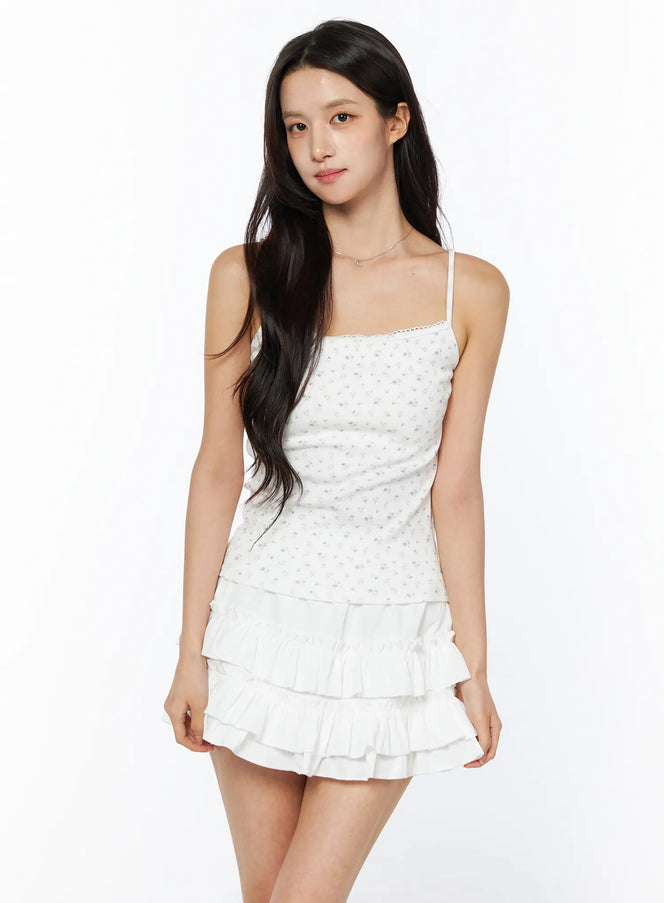 LEWKIN Floral Ribbed Cami Top CU522 in white, front 3/4 view on model, ditsy floral print with lace-trim neckline and thin straps, paired with white tiered ruffle mini skirt.