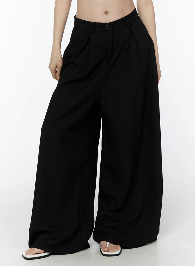 Basic Wide-Leg Slacks IU503 in black, front waist-to-hem close-up on model, pintuck pleats and single-button closure visible, ultra-wide leg, paired with white sandals.
