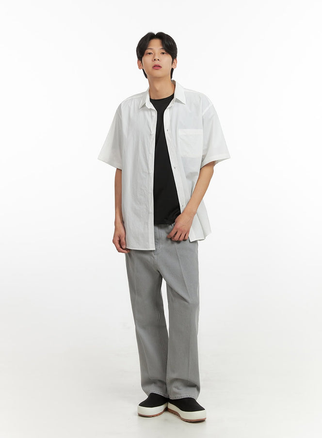 Men's Solid Buttoned Shirt (White) IY431 in white, full-body front view on model, relaxed oversized fit, short sleeves, chest pocket, styled open over black tee with wide-leg grey jeans and black sneakers.