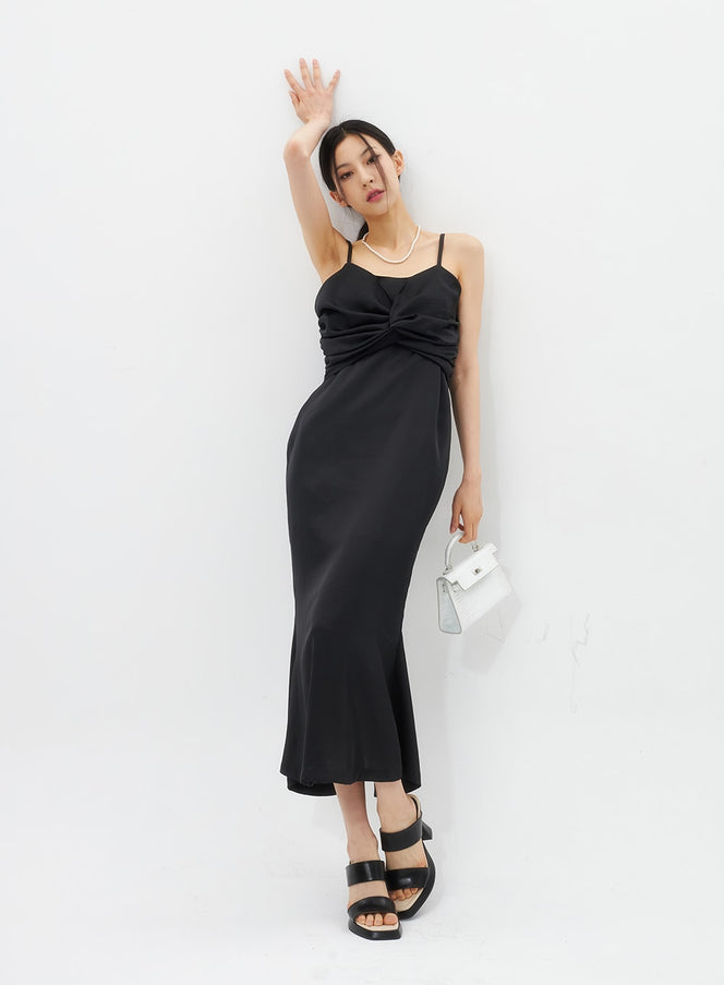 Cross Bust Satin Maxi Dress IU326 in black, front full-length editorial pose, satin slip maxi with gathered cross-bust detail, paired with pearl necklace and white mini bag.