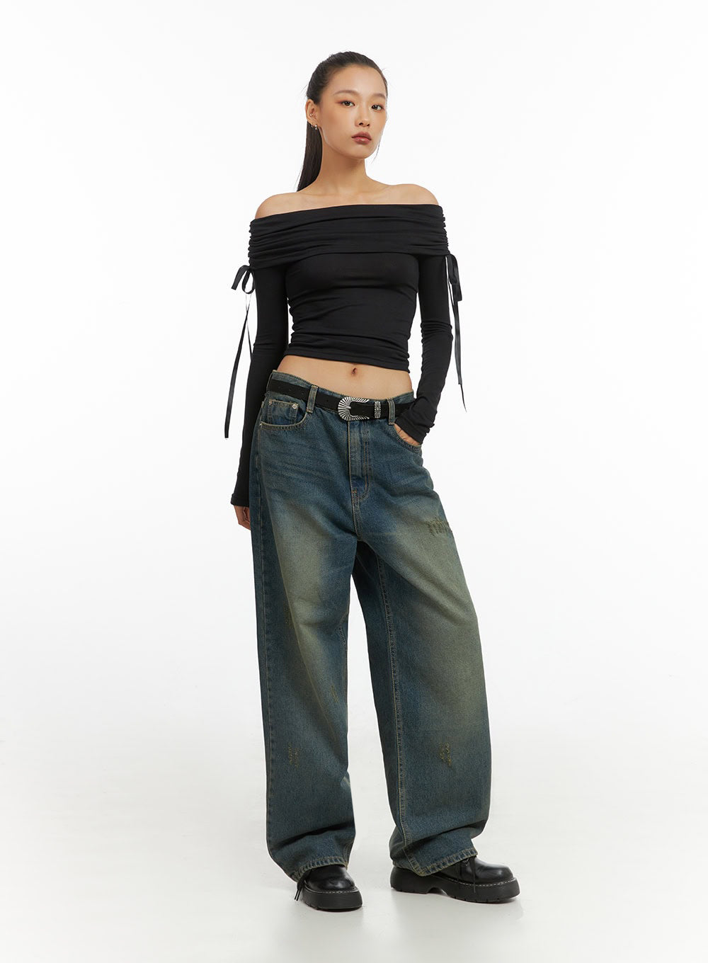 Anya Wide Fit Denim Jeans IO409 in blue, front 3/4 angle on model, baggy washed denim with distressed detailing, paired with black off-shoulder crop top and silver western belt.
