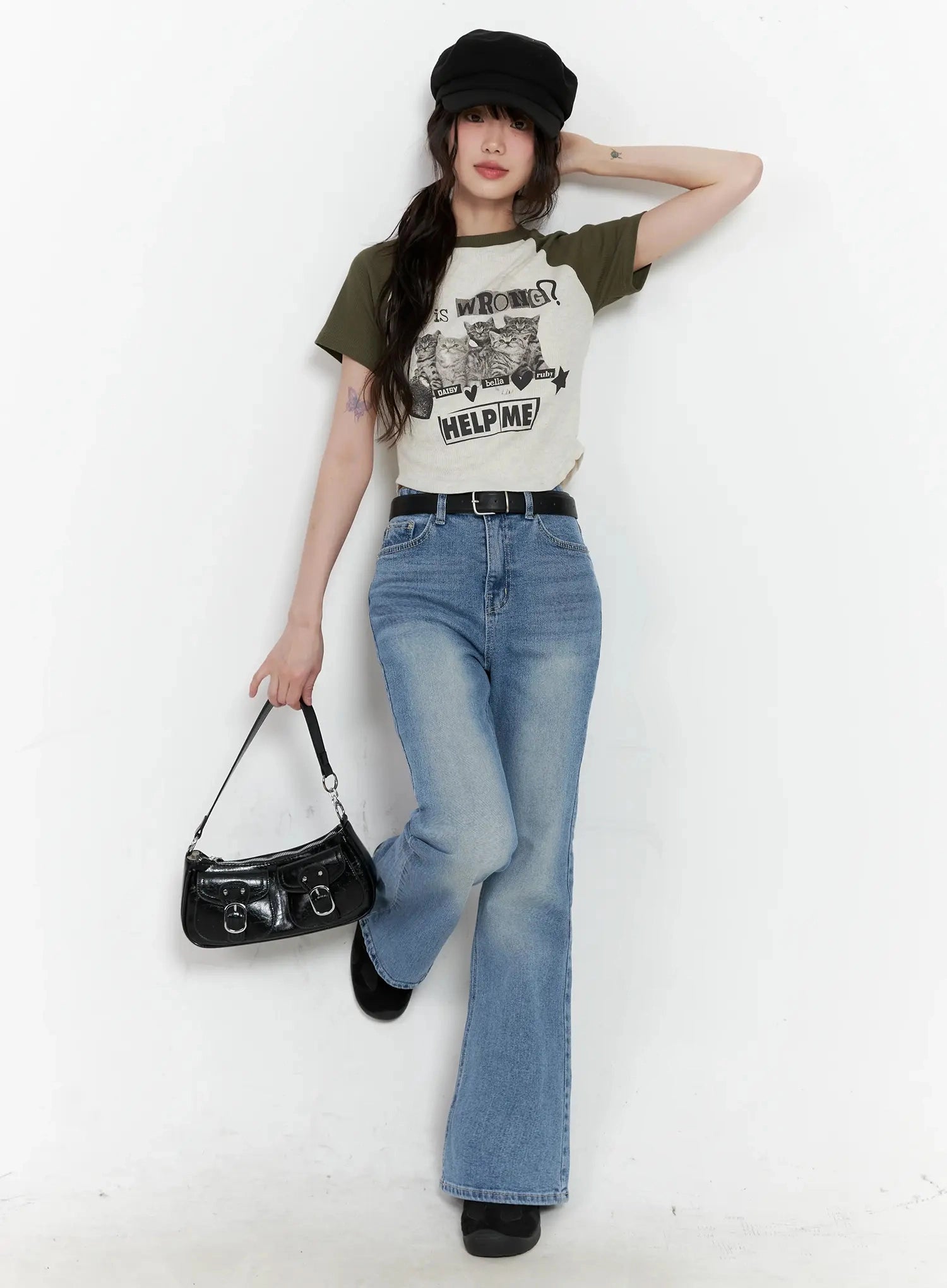 Hikaru High-Waist Flare Jeans IL531 in blue, full-length editorial shot on model leaning against wall, styled with graphic raglan tee, baker boy cap, and black shoulder bag.