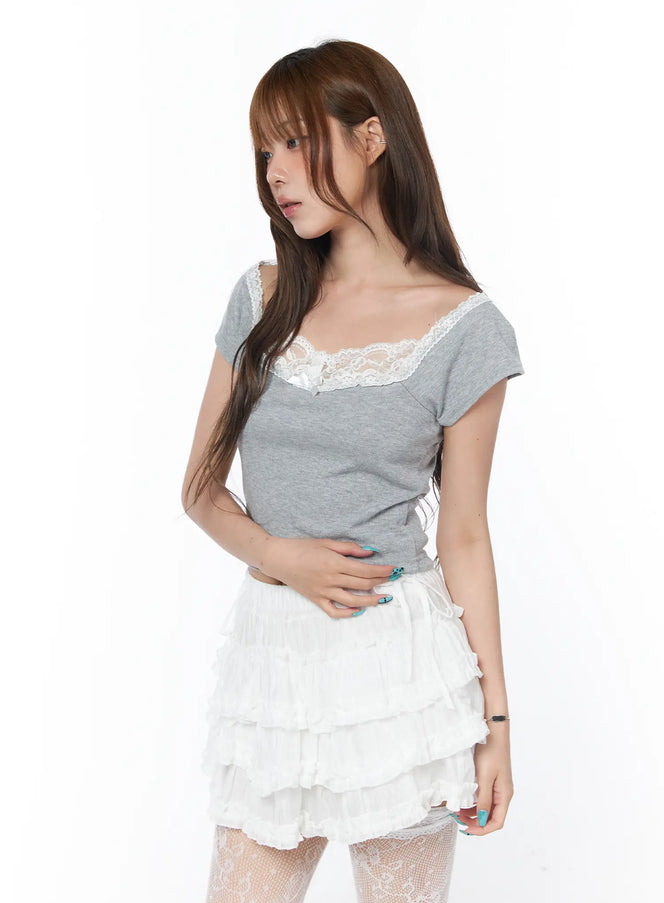 Off-Shoulder Lace Detail Crop Tee CY529 in gray, front angled shot on model, white floral lace off-shoulder neckline, short-sleeve tight crop silhouette, paired with white ruffled mini skirt and lace tights.