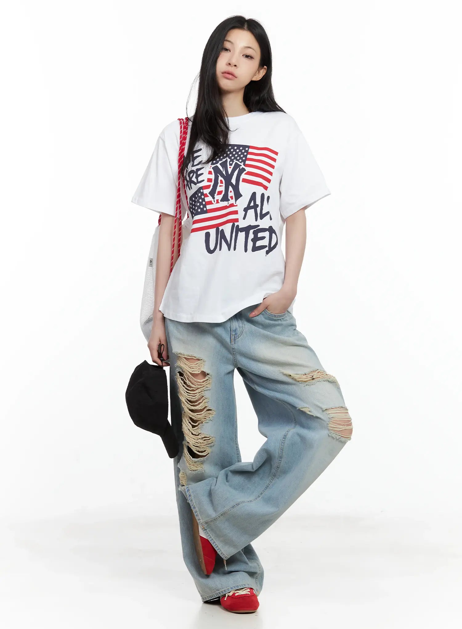 Gyuri Dirty-Wash Distressed Wide Jeans CU530 in blue, full-body front on model, street styling with white graphic tee, holding black cap, wide-leg distressed denim, red flats.