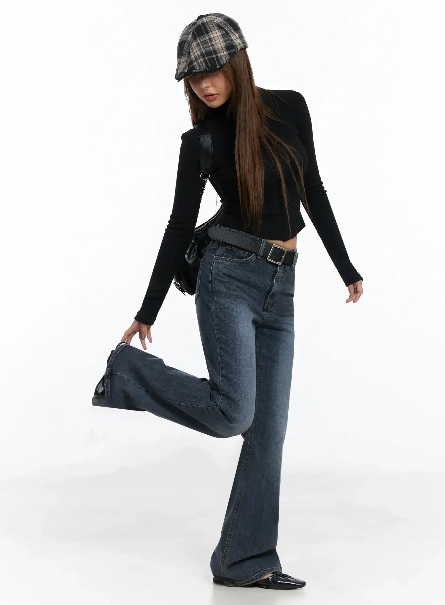 Rara Fleece Flared Jeans ID503 in blue, full-body dynamic pose on model lifting one leg, washed flared hem, styled with black turtleneck, plaid cap, belt, and crossbody bag.