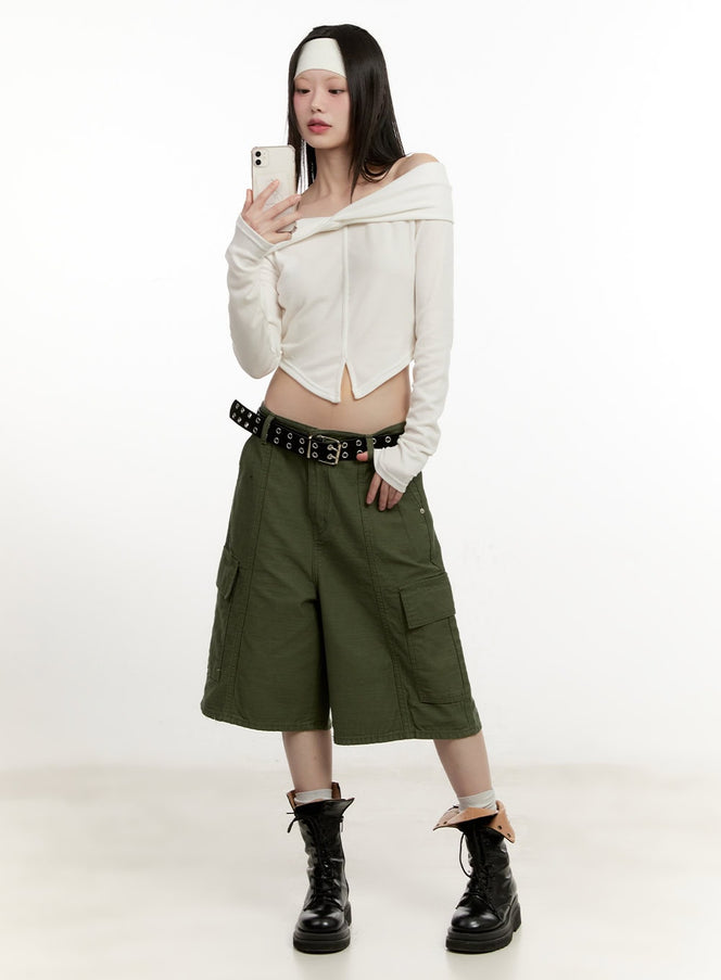 Twist Off-Shoulder Long Sleeve Top CM514 in white, full-body front shot on model holding phone, cropped slim fit with off-shoulder neckline, styled with green cargo shorts and combat boots.