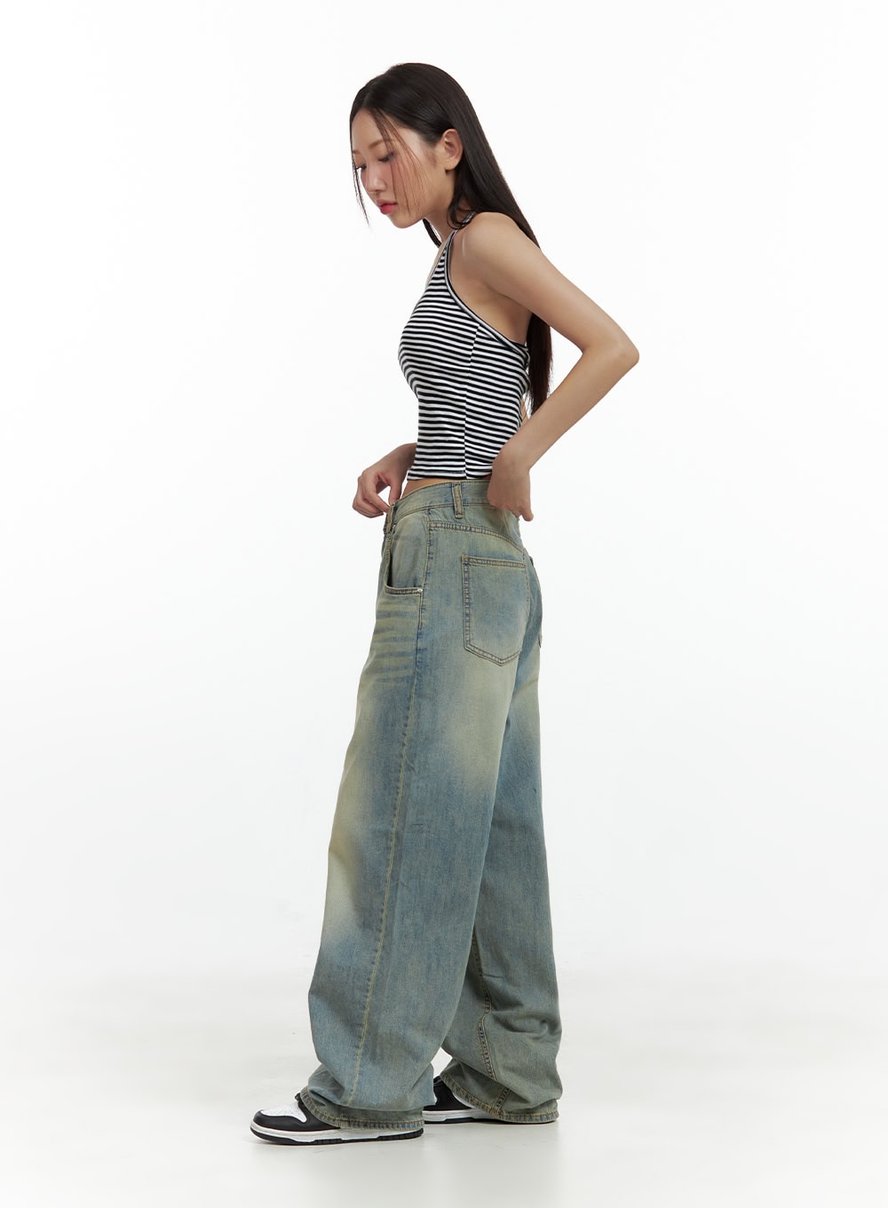 Relaxed Wide-Leg Jeans CU420 in blue, side full-length view on model, washed denim with vintage yellow fade, ultra-wide leg pooling at sneakers, styled with striped halter crop top.