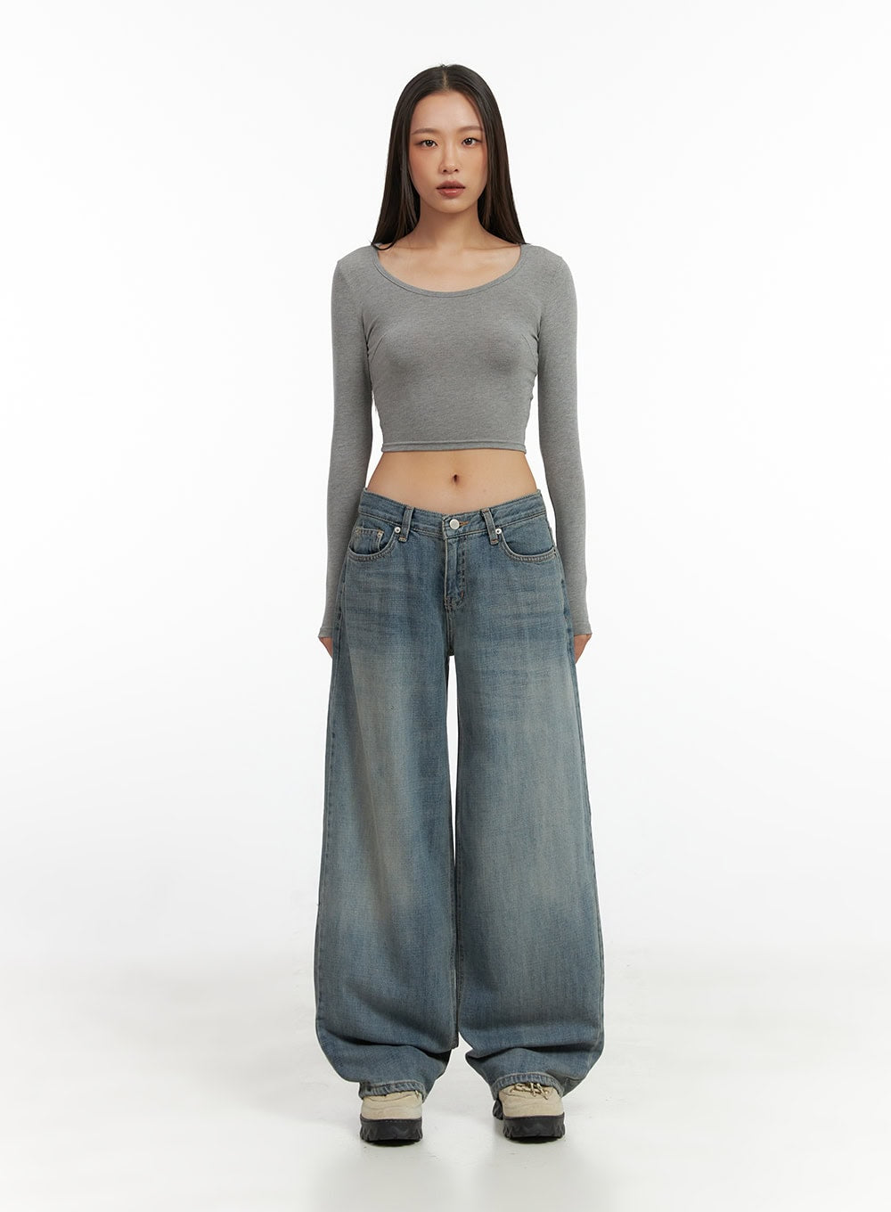 Nadia Washed Low-Waist Baggy Jeans CO424 in blue, full-body front shot on model, ultra-wide baggy leg pooling at hem, styled with grey long-sleeve crop top and beige chunky sneakers.