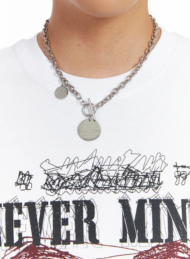 Men's Steel Chain Necklace IL518 in silver, chest-level close-up on model, chunky cable chain with toggle clasp and dual engraved coin charms, styled over white graphic tee.