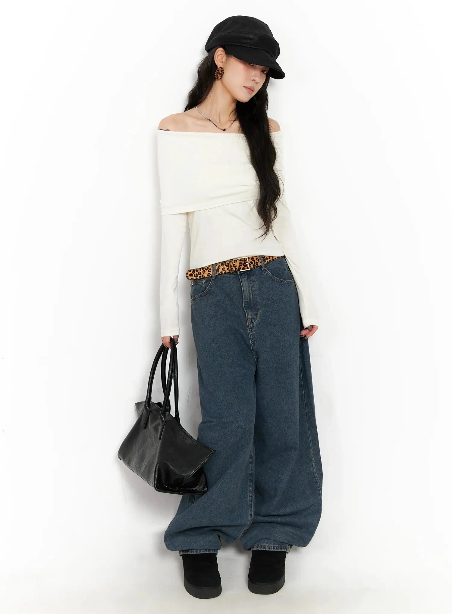 Aleena Mid-Wash Baggy Jeans IN528 in dark blue, full-length side-angled shot on model wearing white off-shoulder top, leopard belt, black cap and tote bag.