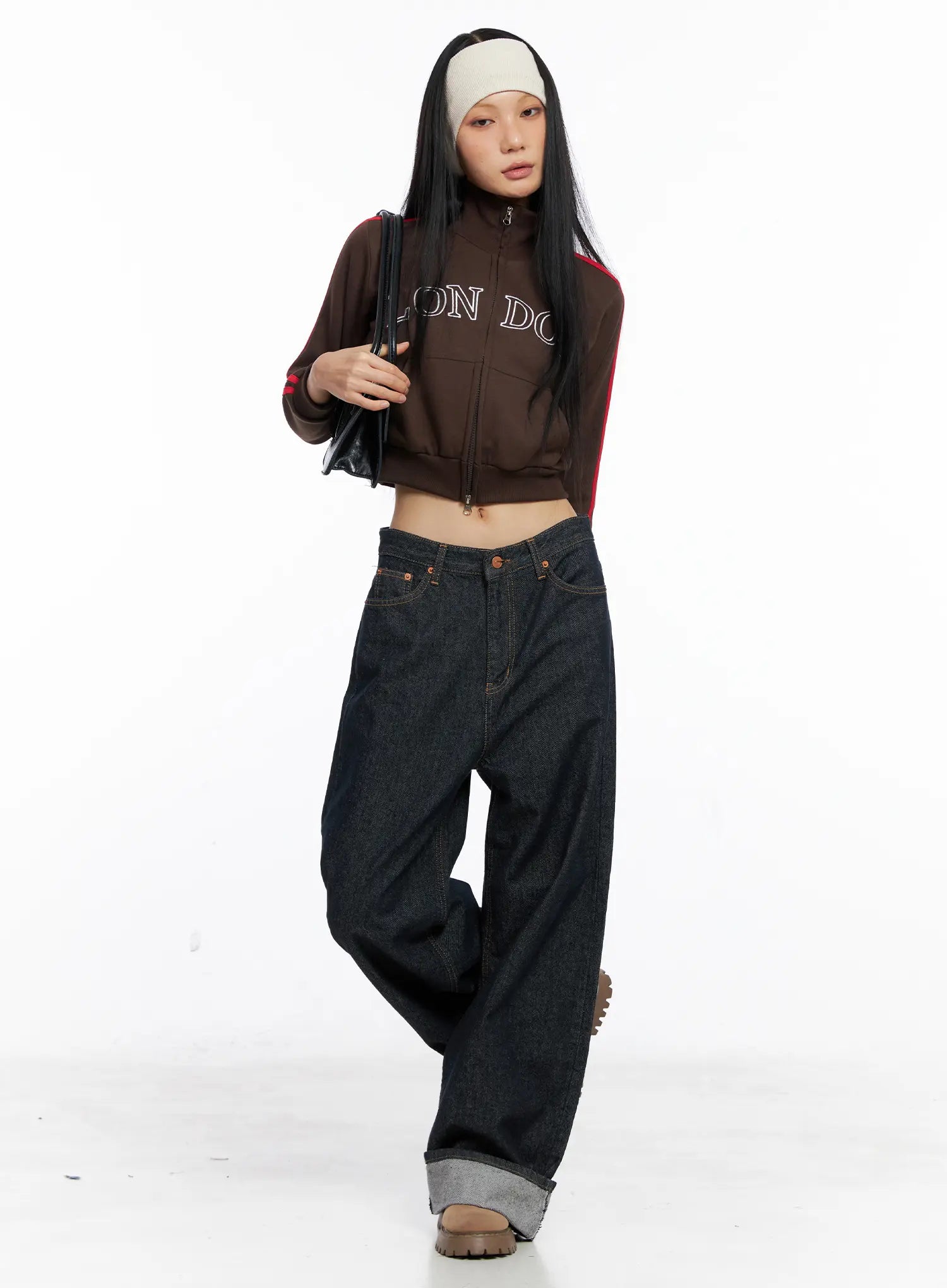 Oakley Cuffed Wide-Leg Jeans CS511 in dark blue, full-length styled shot, model in motion wearing brown crop track jacket, headband, and chunky boots, wide-leg roll-up hem visible.