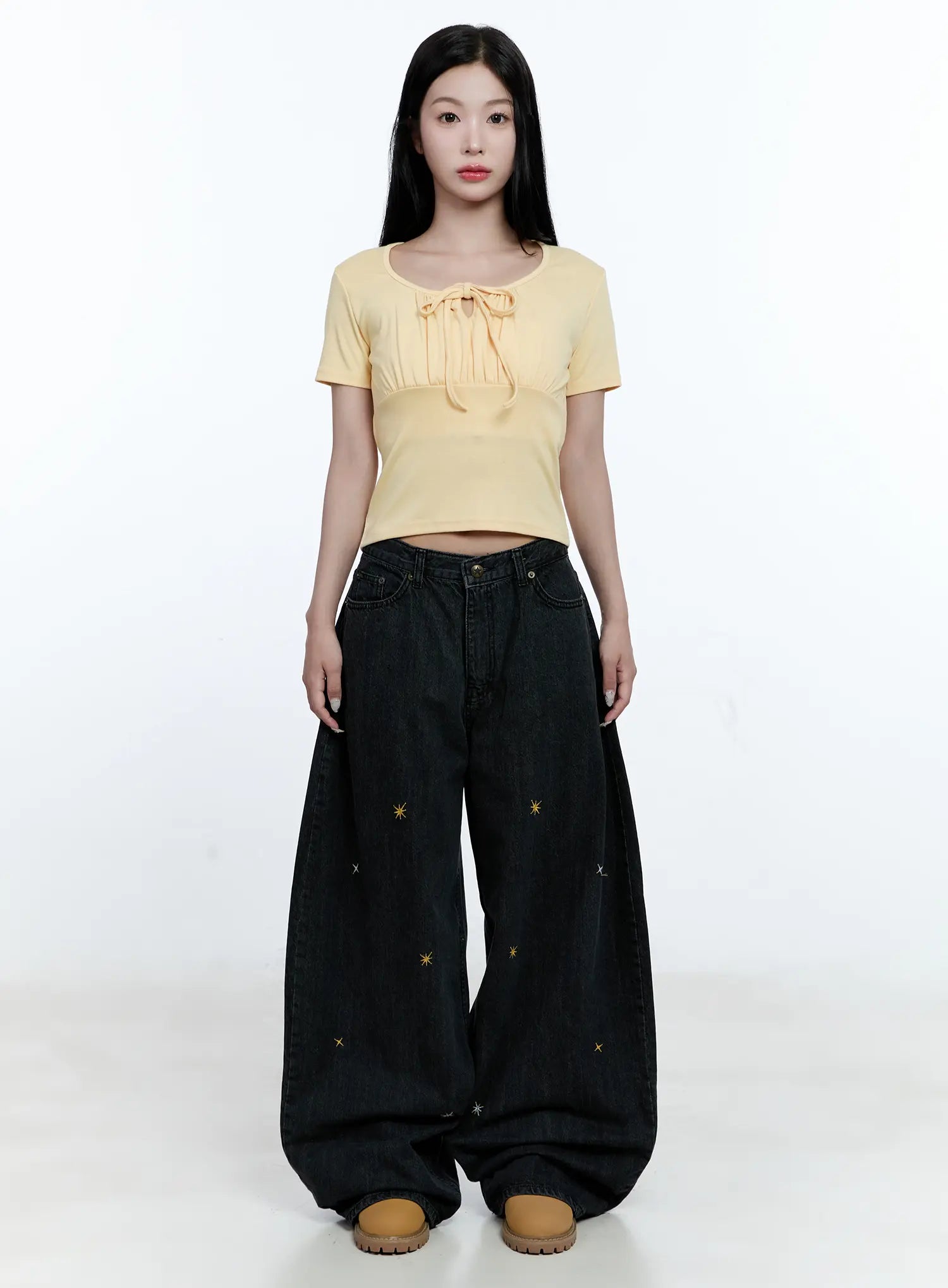 Wynter Star Embroidered Denim Jeans CG507 in black, full-body front on model, ultra-wide pooling leg silhouette with star embroidery, styled with a yellow bow crop top and tan platform shoes.