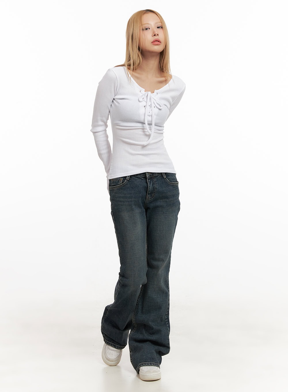 Natalia Low-Rise Flared Jeans CJ508 in dark blue, full-length front view on model walking, slim low-rise washed denim with flared hem, styled with white lace-up ribbed top and white sneakers.