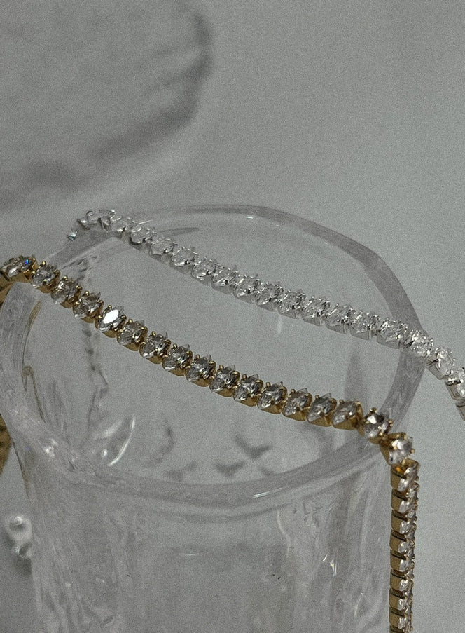 All Square Cubic Bracelet IL411 in gold and silver, close-up detail draped over crystal glass, sparkling square cubic zirconia links clearly visible.