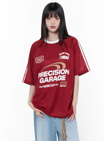 Oversized Sporty Graphic Tee CU519 in red, front view on model, mesh texture with white side stripes, Precision Garage racing graphic, paired with wide-leg light blue jeans and belt bag.