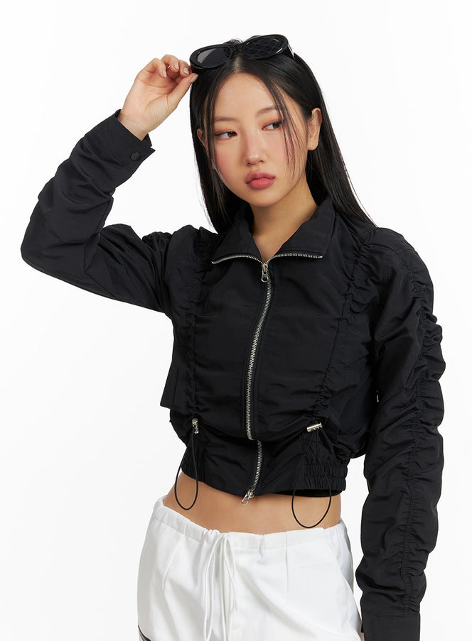 Shirred Nylon Crop Jacket CF414 in black, front close-up on model, showcasing full-length zipper and shirring detail on sleeves and body, paired with white pants.