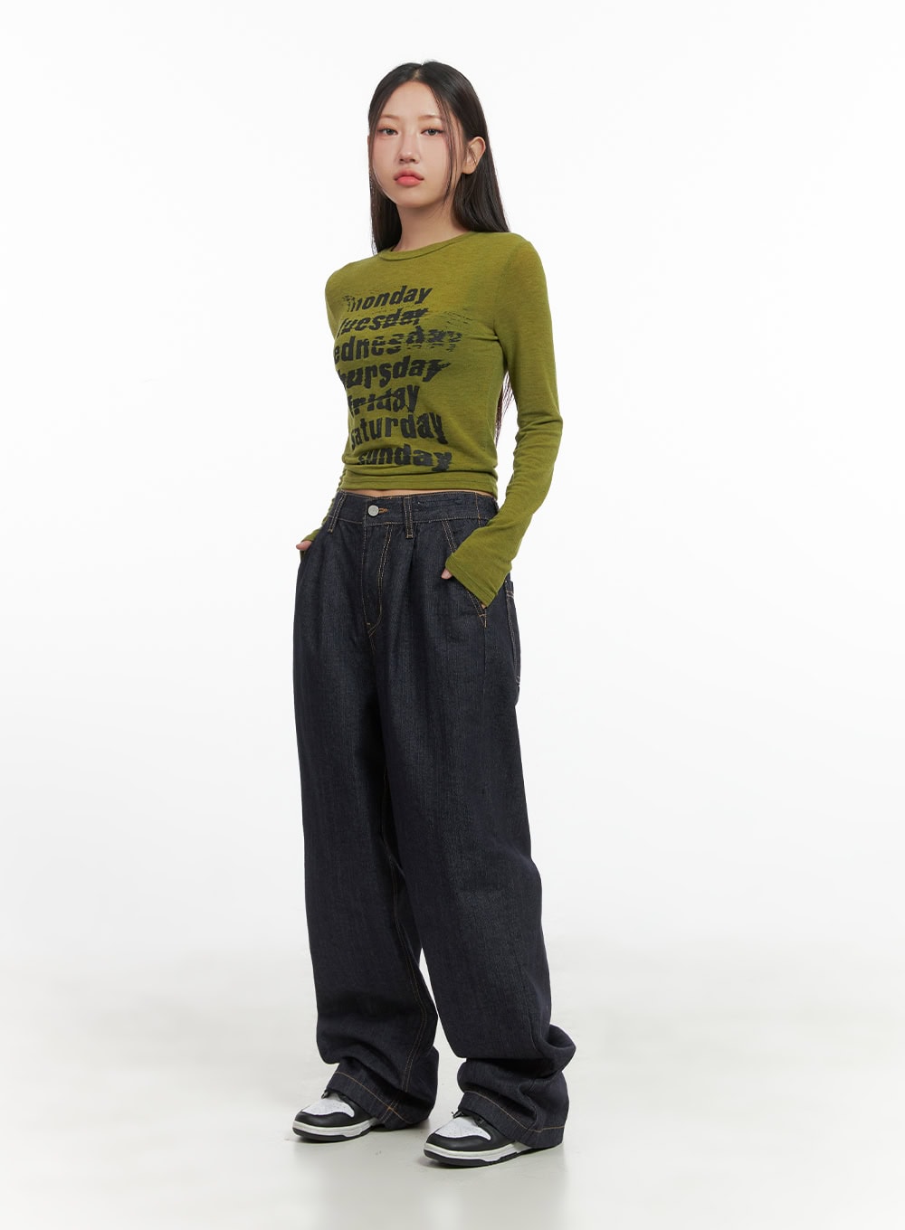 Lola Pintuck Baggy Jeans CO402 in dark blue, full-body front shot on model, wide-leg silhouette pooling at hem, paired with olive days-of-week crop long sleeve and chunky sneakers.