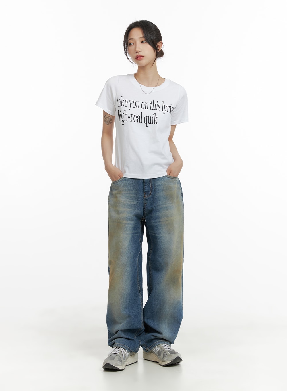 Vintage Washed Baggy Jeans CM426 in blue, full-body front shot on female model, wide baggy fit with vintage yellow-tinted wash, styled with white graphic tee and grey sneakers.