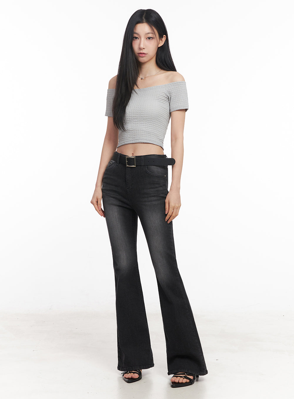 Lior Slim-Fit Bootcut Jeans IY516 in black, full-length front shot on model, belted high-rise washed bootcut denim, styled with grey off-shoulder crop top and black strappy heels.