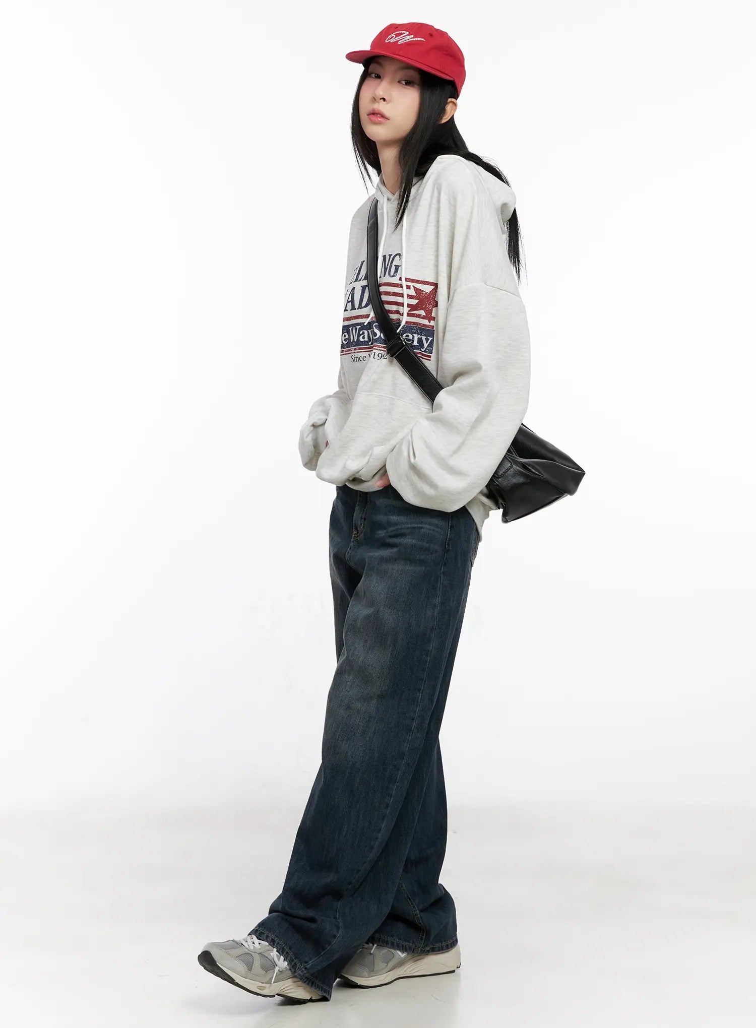Seoy Washed Denim Jeans CG525 in dark blue, full-body angled shot on model, styled with grey graphic hoodie, red cap, and black crossbody bag, street casual look.