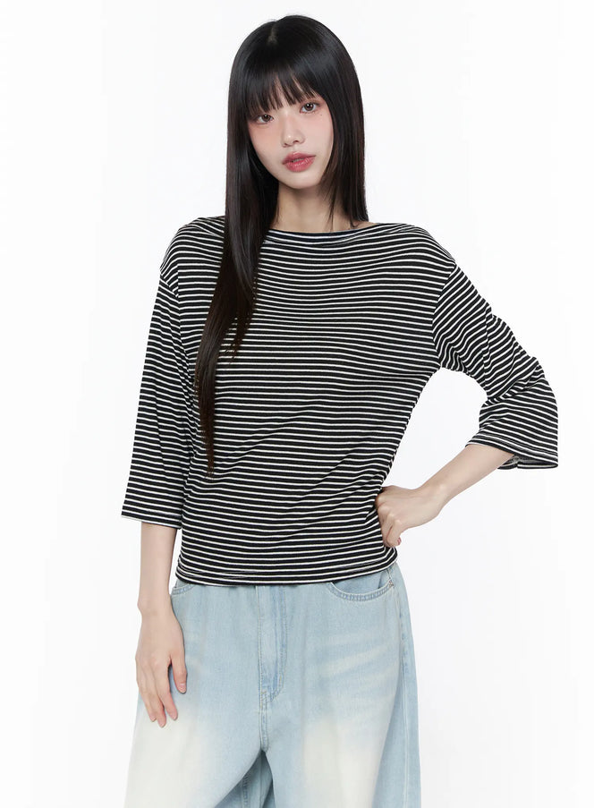 Striped Boat Neck Long Sleeve Tee CU519 in black, front view on model with hand on hip, wide boat neckline, relaxed boxy fit with horizontal stripes, styled with light blue wide-leg jeans.