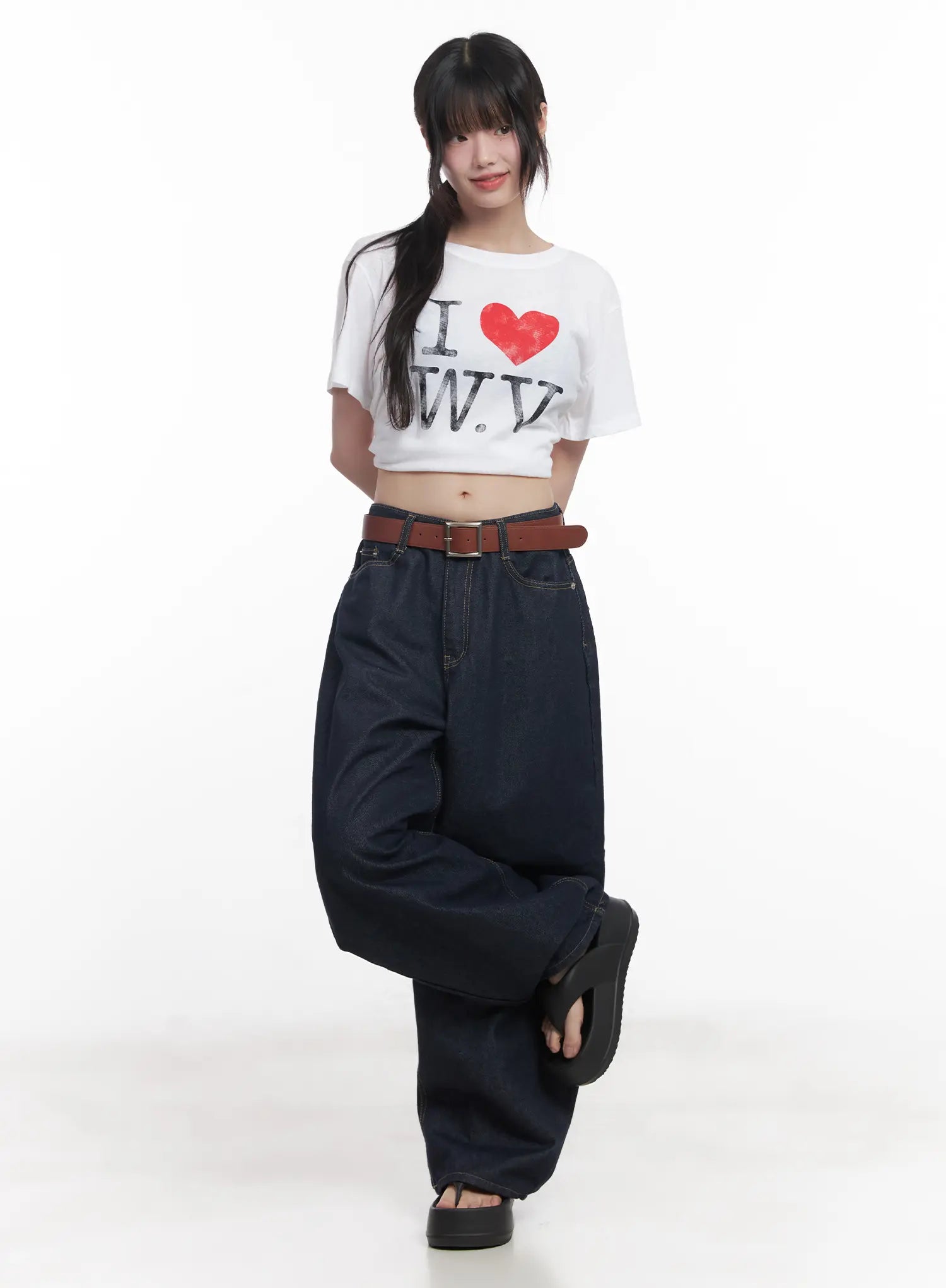 Hyein No-Fade Relaxed-Fit Jeans CU519 in dark blue, full-body front shot on model, wide-leg silhouette with brown belt, styled with white graphic crop tee and black sandals.