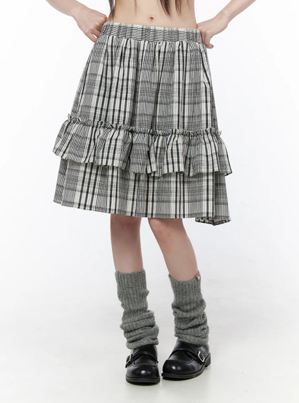 Plaid Layered Midi Skirt CU519 in black, front view on model, double-tiered ruffle hem, smocked elastic waistband, black-white plaid, paired with grey leg warmers and Mary Jane shoes.