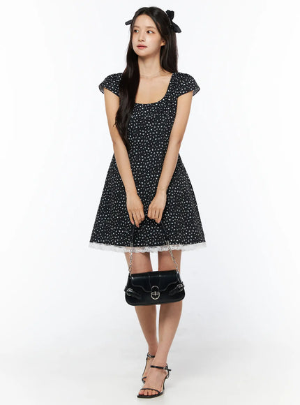 Floral Lace Trim Mini Dress CU522 in black, full-length front view on model holding black shoulder bag, lace trim hem detail, cap sleeves, paired with strappy heels.