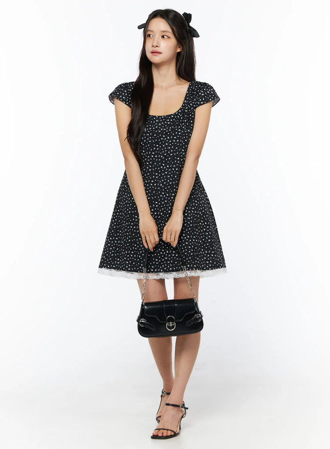 Floral Lace Trim Mini Dress CU522 in black, full-length front view on model holding black shoulder bag, lace trim hem detail, cap sleeves, paired with strappy heels.