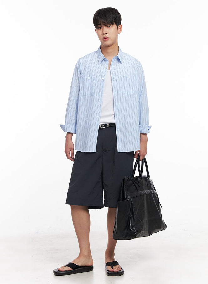 Men's Striped Collared Shirt IY522 in light blue, full-body front on model, sleeves rolled, open over white tee, styled with navy bermuda shorts, sandals, and large black tote bag.