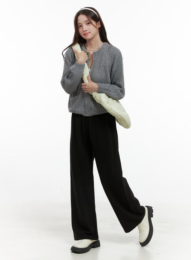 Warm Knit Zip-Up Cardigan OS416 in gray, full-body shot on model holding cream quilted bag, styled with black wide-leg trousers and white boots.