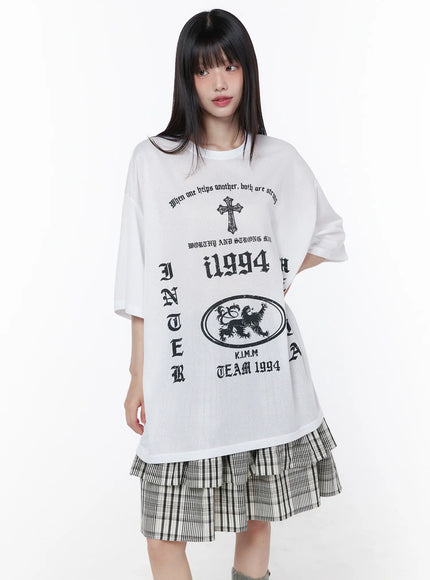 Oversized Mesh Graphic Tee CU519 in white, front full-body shot on model, semi-sheer mesh fabric with black gothic cross, i1994 and lion crest prints, styled over plaid tiered mini skirt.