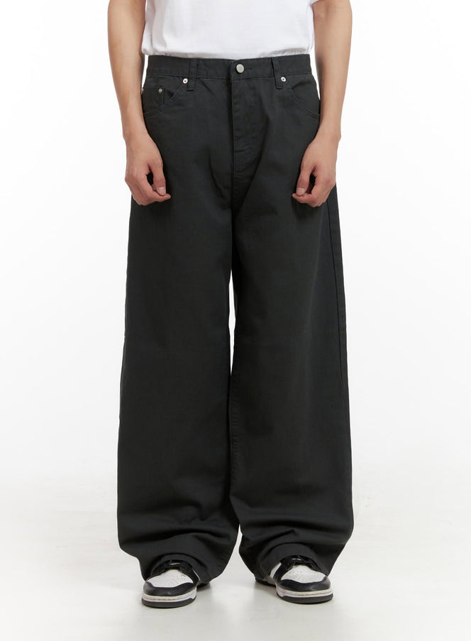Men's Solid Cotton Baggy Pants IL404 in dark gray, front close-up on model, ultra-wide leg with 5-pocket design, button fly, and stacked hem over black-and-white sneakers.