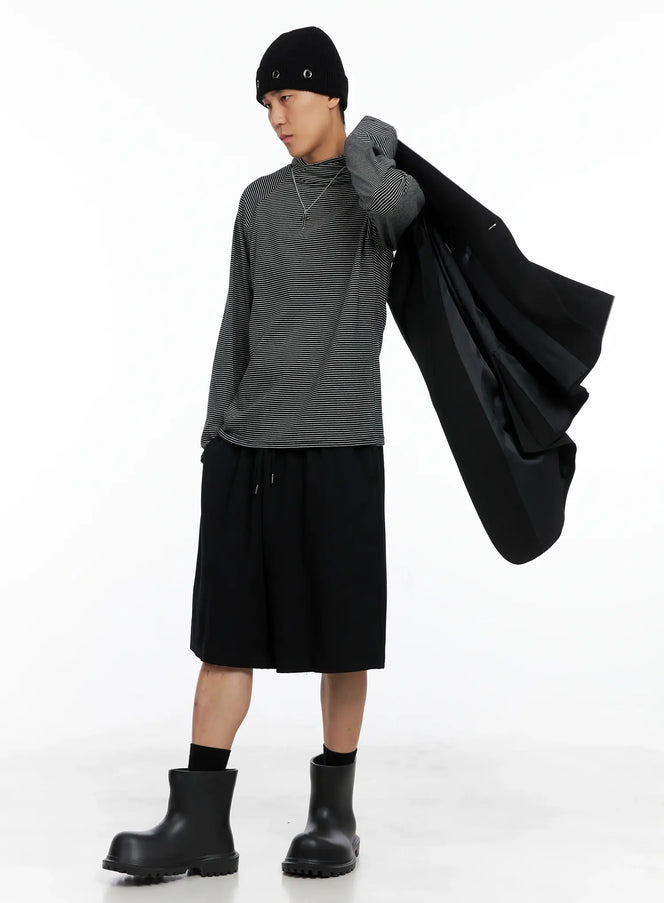 Men's Striped Long Sleeve Hoodie IS502 in black, three-quarter front view, model draping black coat over shoulder, slim raglan sleeves, worn with wide-leg shorts.