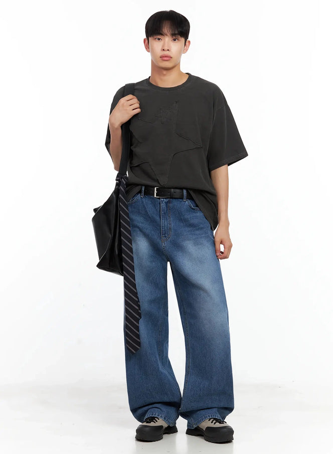 Men's Star Patch T-Shirt IL516 in black, full-body styled shot, model holding black tote bag with striped tie, worn with wide-leg blue jeans and chunky sneakers.