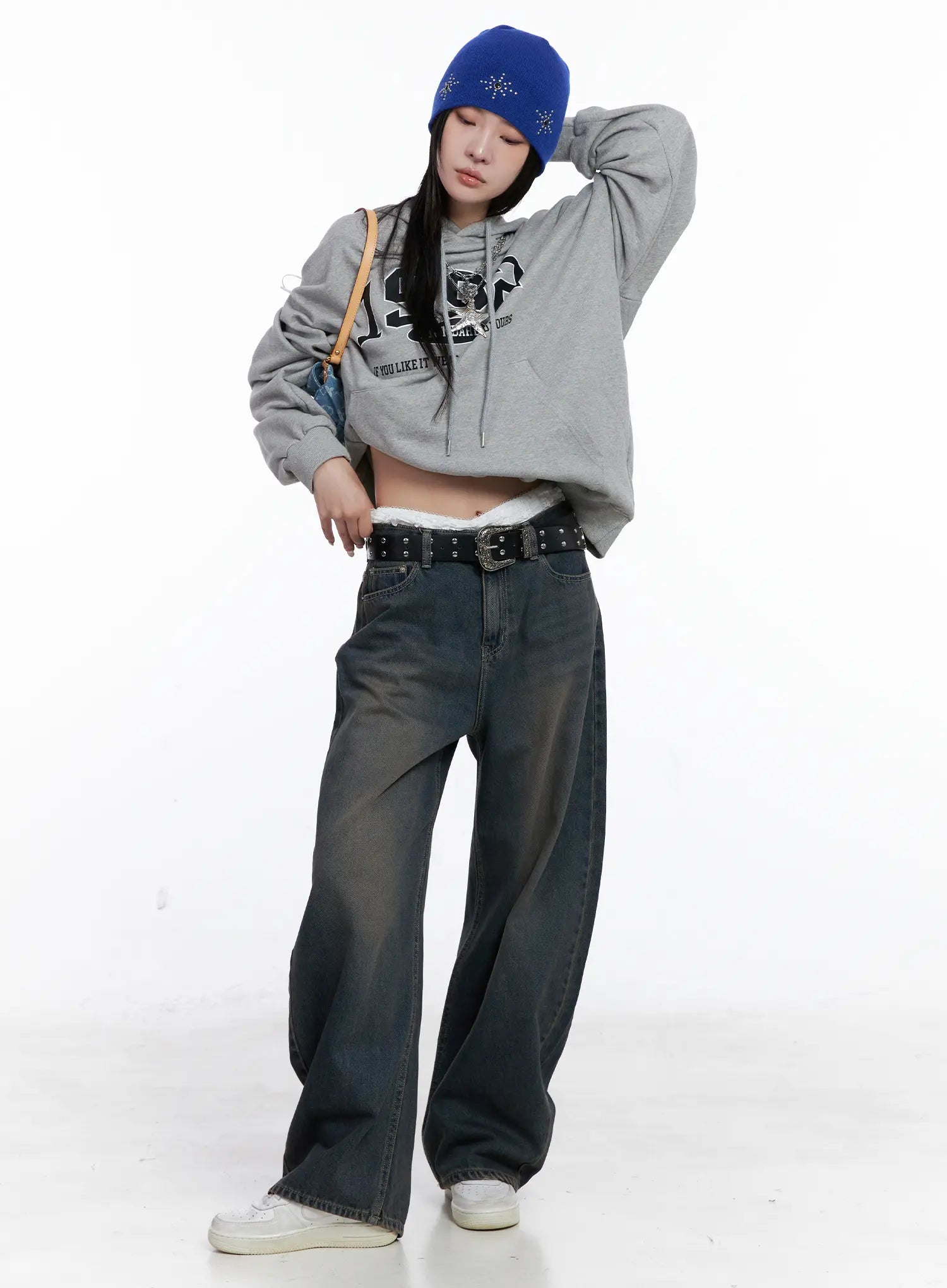 LEWKIN Ocean Faded Balloon Fit Jeans CS510 in washed dark indigo, full-length front shot on model, wide balloon silhouette with studded belt, styled with grey crop hoodie, blue beanie, and white sneakers.