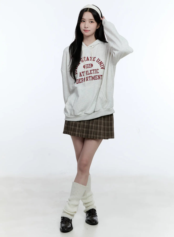 Classic School Girl Pleated Skirt CG514 in brown, full-body front shot on model, preppy K-pop styling with oversized college hoodie, cream leg warmers and black loafers.
