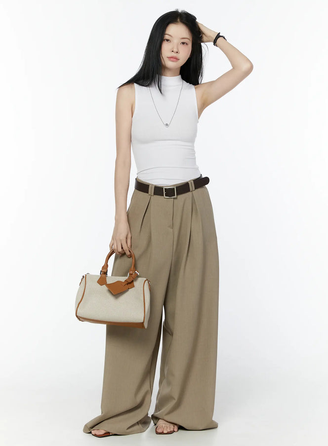 Classic Wide-Fit Pleated Pants IU503 in beige, full-length front editorial shot on model, styled with white sleeveless top, brown belt, and structured canvas tote bag.